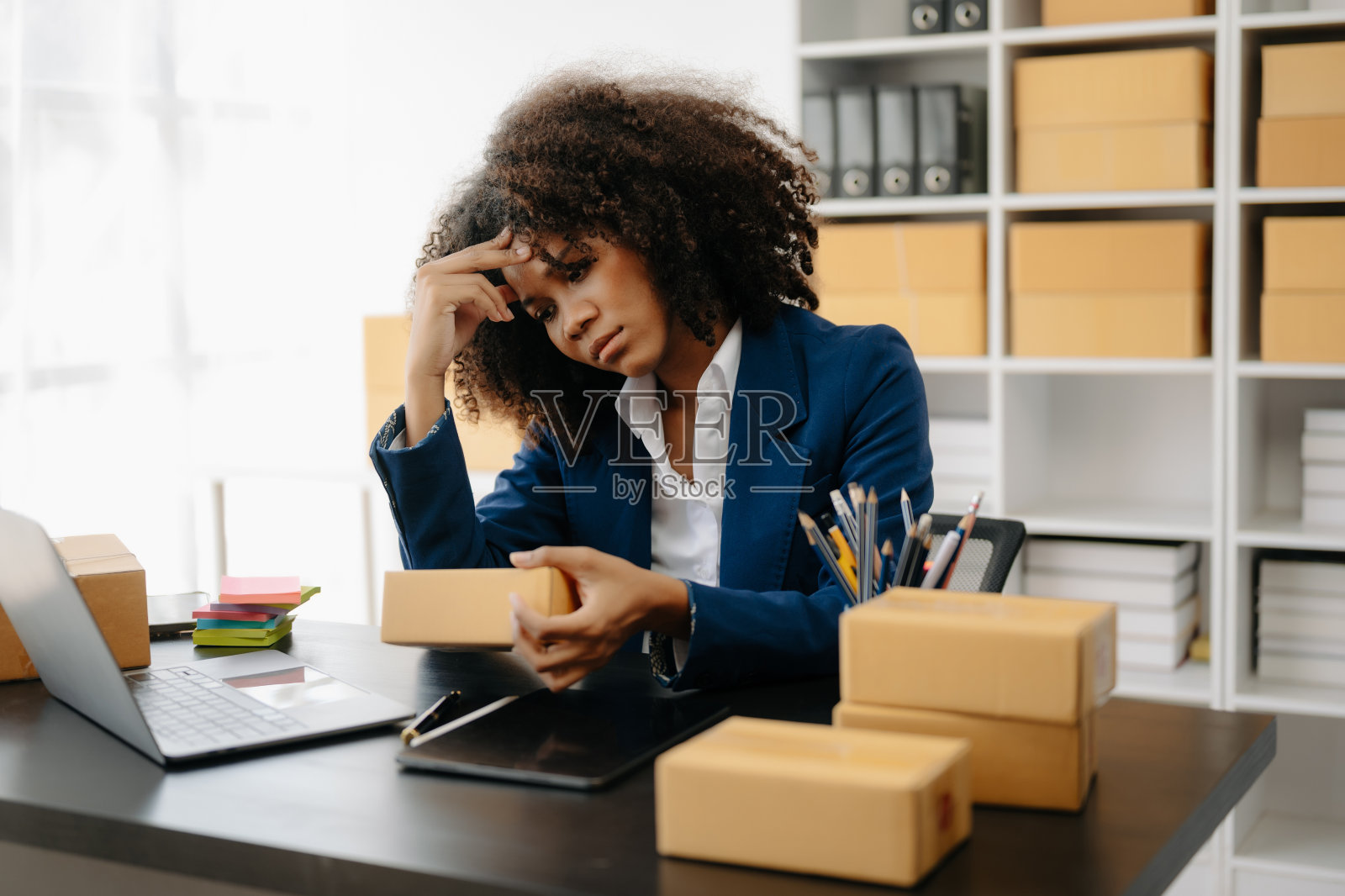 创业小型企业中小企业,企业家老板非洲妇女使用智能手机或平板电脑接收和检查网上购物订单,准备包装产品盒。照片摄影图片