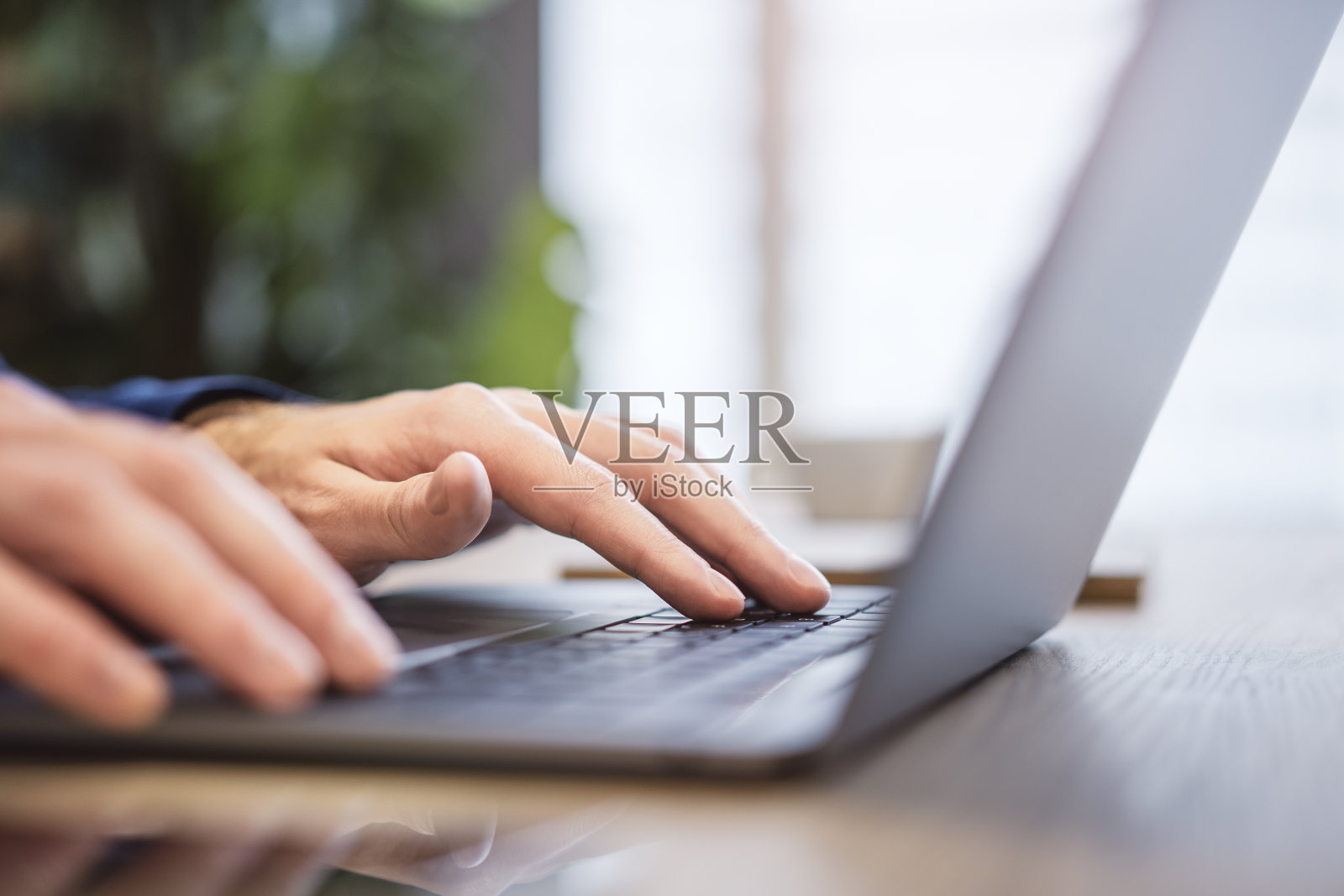 在一个模糊的办公室背景下,一个男人的手在一个光滑的笔记本电脑键盘上打字照片摄影图片