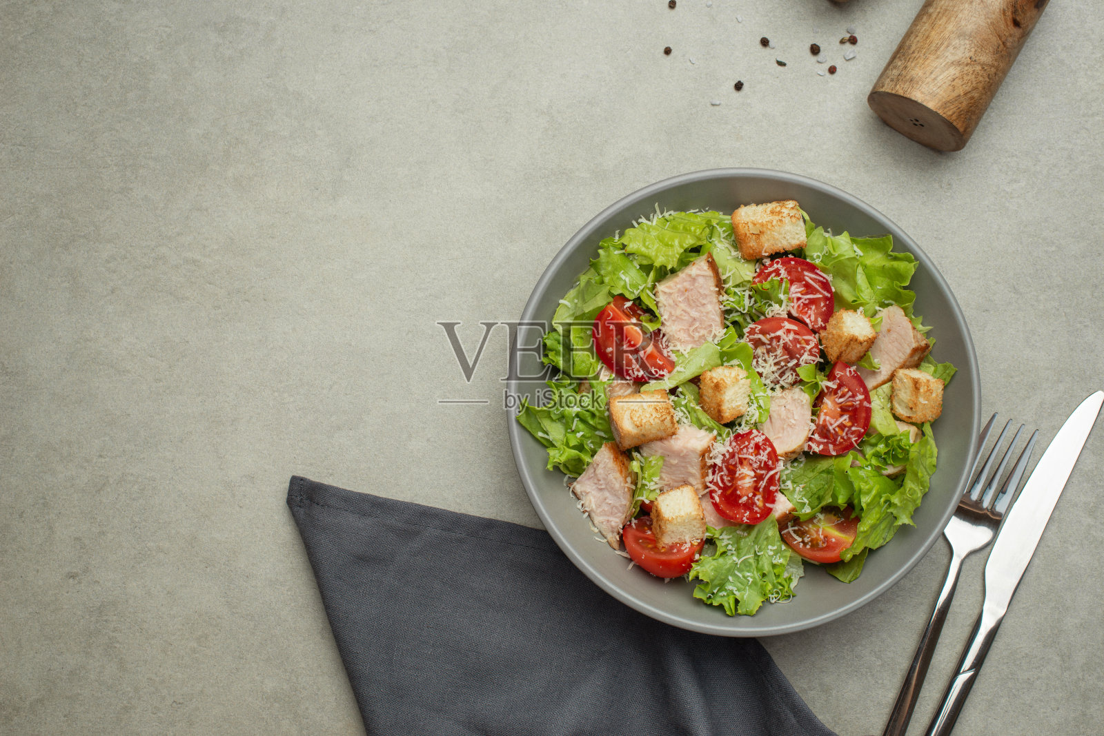 灰色桌子上的蔬菜沙拉配鸡肉和奶酪。灰色盘子里的凯撒沙拉。照片摄影图片