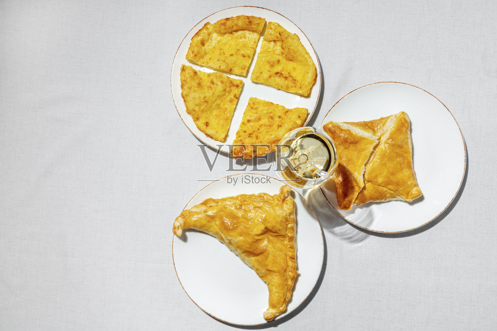 三种类型的khachhapuri,奶酪,羊肉和suluguni,躺在明亮的陶瓷盘子里。旁边放着一瓶酒,透明的玻璃杯高脚上放着白葡萄酒。盘子放在一块轻薄的亚麻布桌布上。照片摄影图片