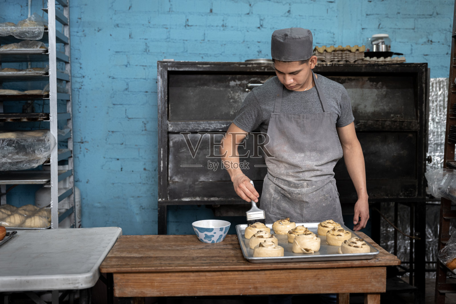 一位年轻的西班牙面包师在烘烤前给肉桂卷上鸡蛋釉照片摄影图片