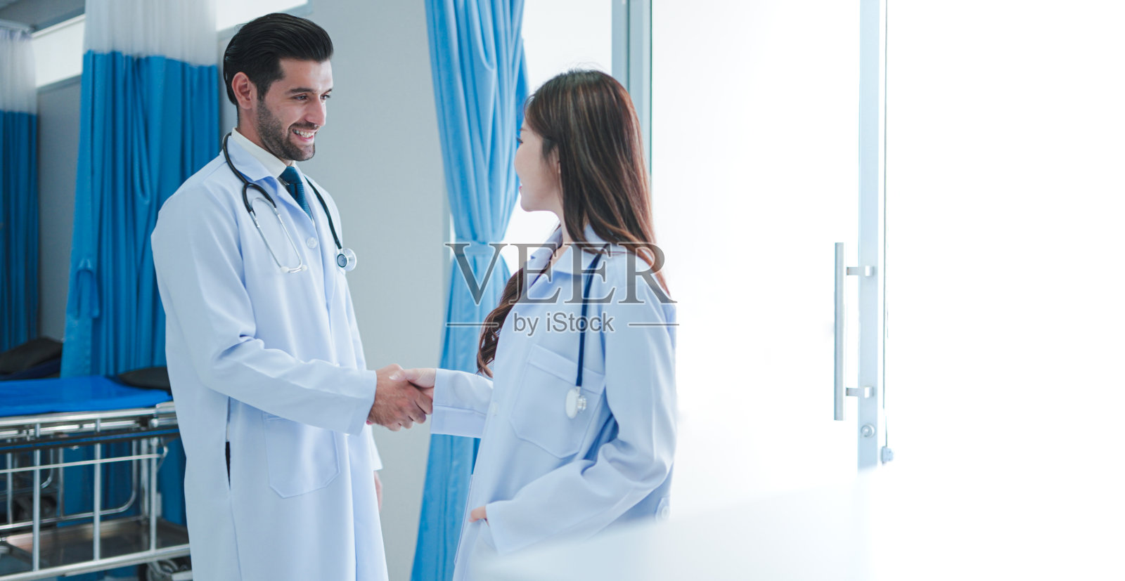 男医生和亚洲女医生在医院走路和问候与握手同事站着谈话讨论。照片摄影图片