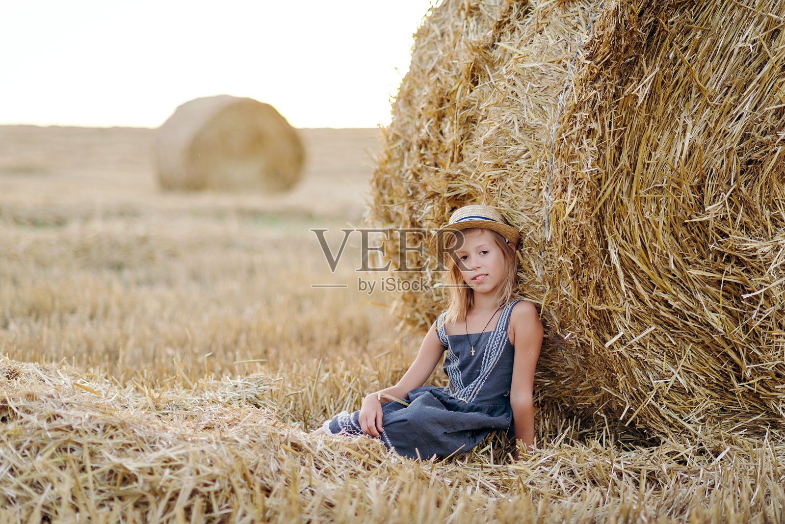 可爱的高加索女孩喜欢坐在农场附近收获小麦的金色干草捆下玩。快乐的童年和自由的观念。乡村风景照片摄影图片