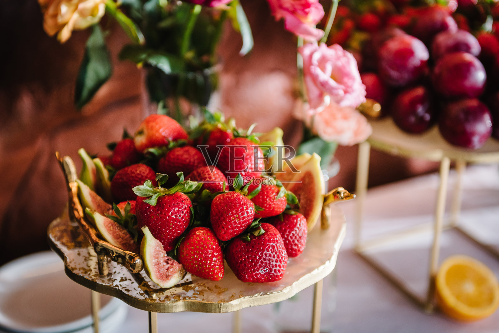 一盘水果,草莓,李子,无花果。糖果棒特写。美味的婚宴豪华的仪式。背景装饰。餐桌上装饰着粉红色的玫瑰,用于生日宴会。照片摄影图片