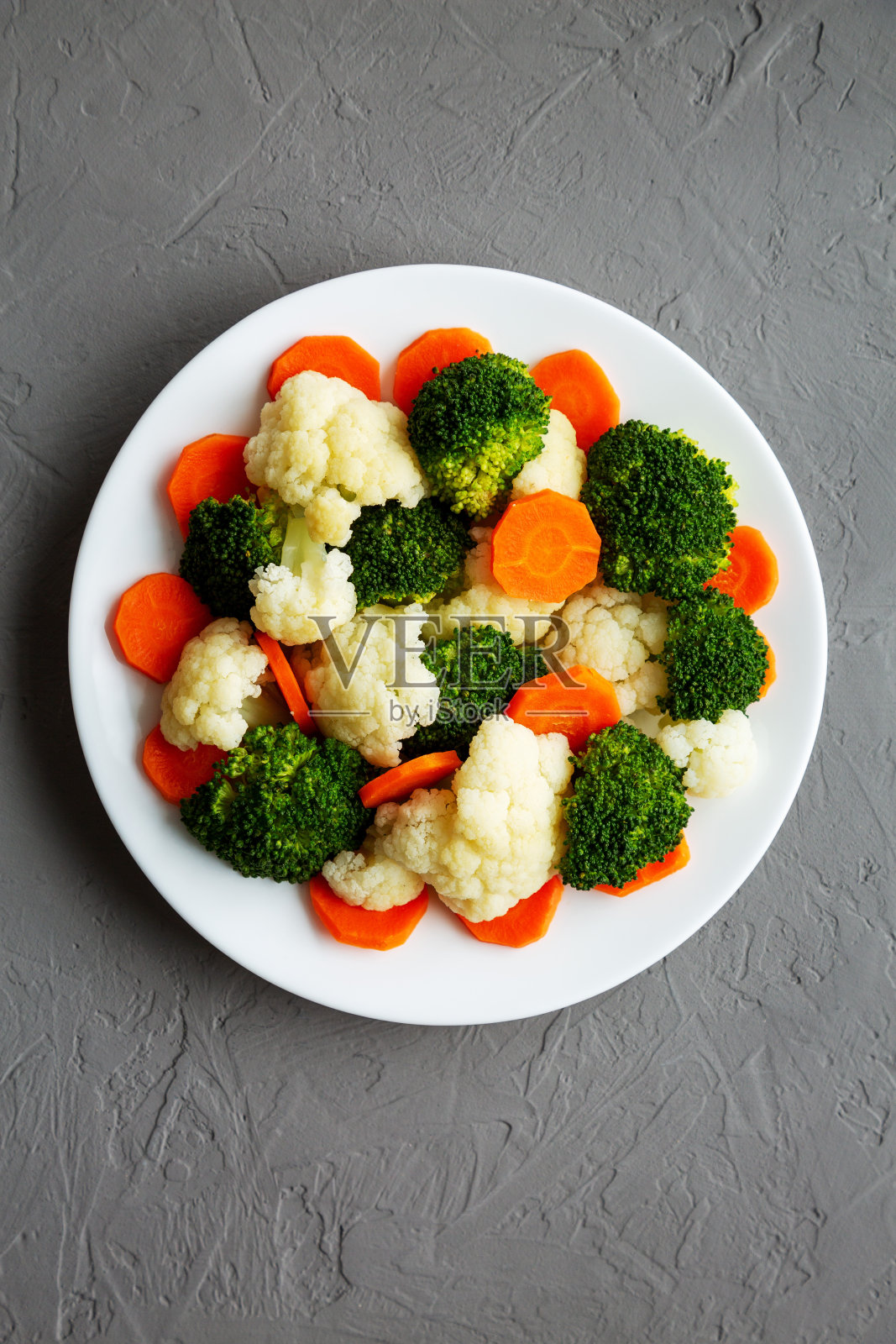 混合有机蒸蔬菜(胡萝卜,西兰花和花椰菜)在一个灰色表面的盘子上,俯视图。平躺,头顶,从上面看。照片摄影图片