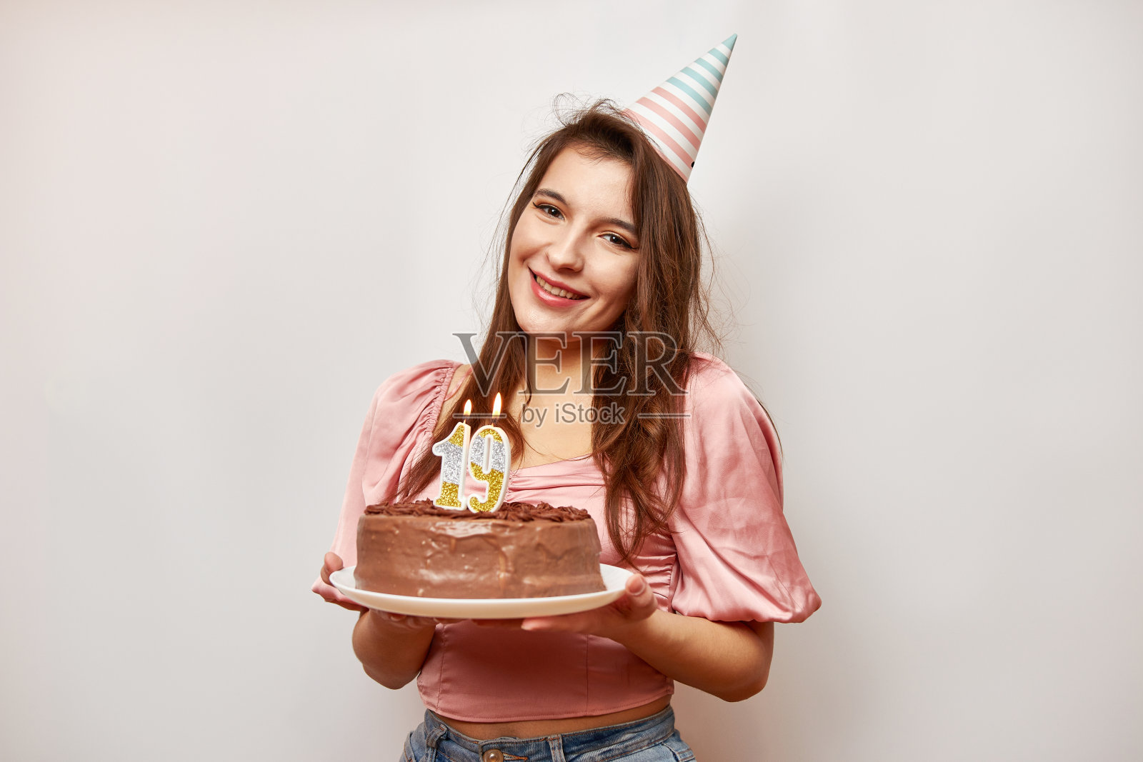 这个女孩拿着一个节日蛋糕,上面插着数字19形状的蜡烛。生日庆祝的概念。照片摄影图片