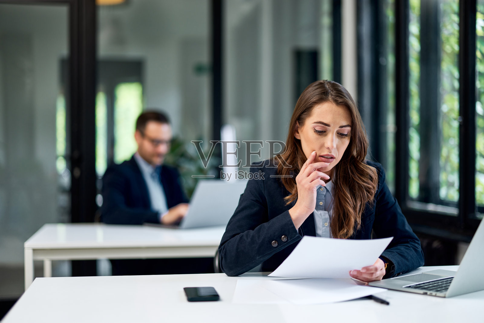 一位女商人正在阅读文件,一位男同事坐在她后面。照片摄影图片