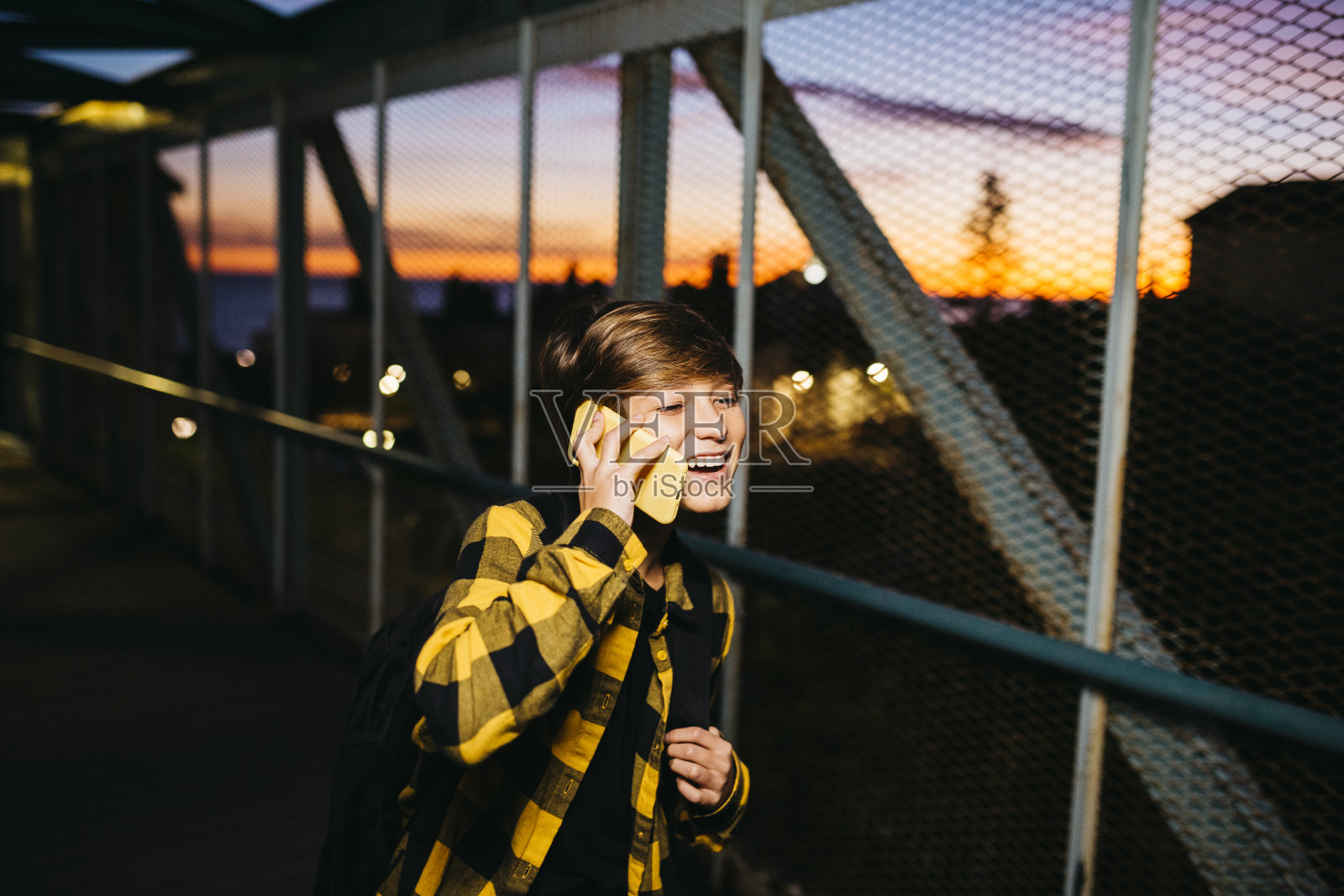 一个十几岁的男孩用智能手机穿过一座金属桥照片摄影图片