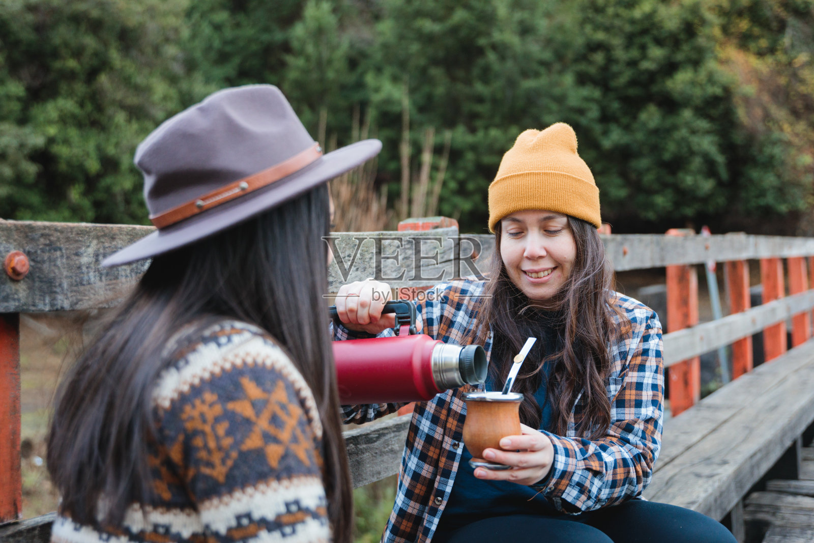 快乐的年轻妇女在农村一起享受马黛茶,裹着温暖的衣服。照片摄影图片