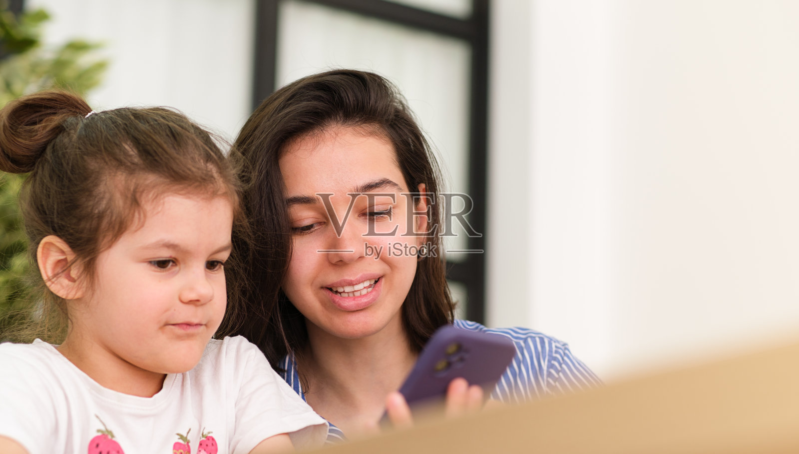 幸福的家庭,可爱的小孩,女儿和妈妈,笑,用智能手机,在社交软件上看搞笑视频,自拍,在家看手机屏幕照片摄影图片