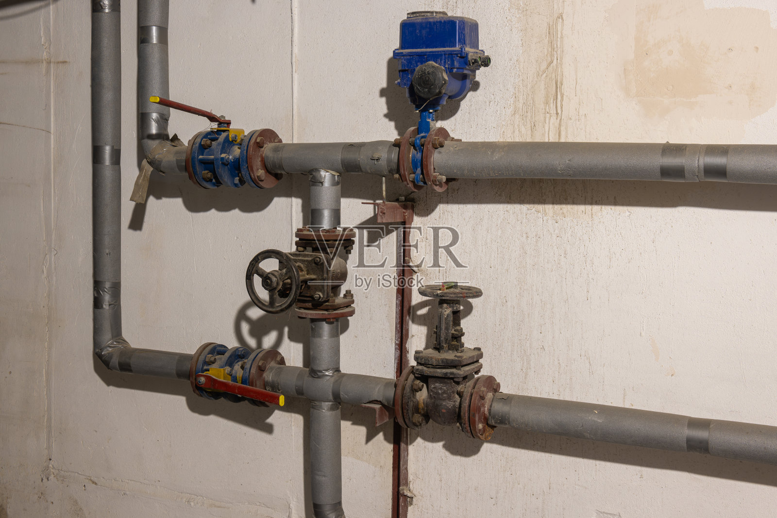 布满灰尘的旧地下室里的供暖系统。加热管道、阀门、泵照片摄影图片