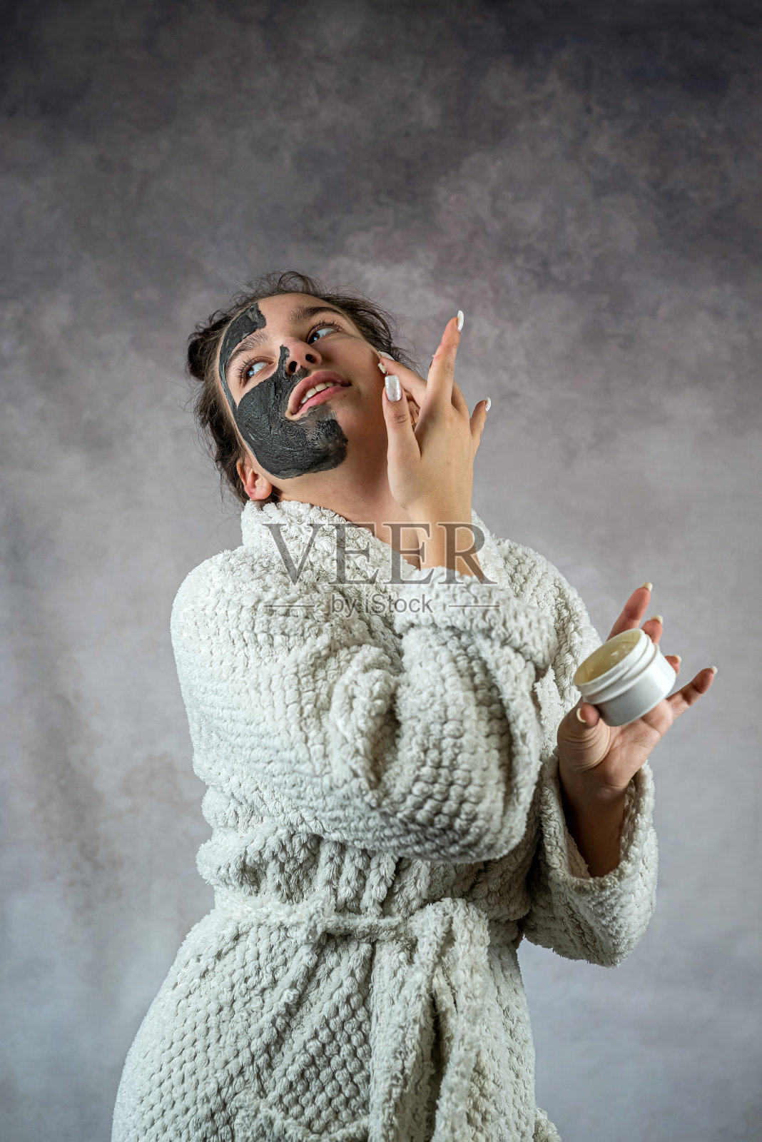 漂亮的年轻女子戴着黑色的面膜,手里拿着装着奶油的塑料瓶照片摄影图片