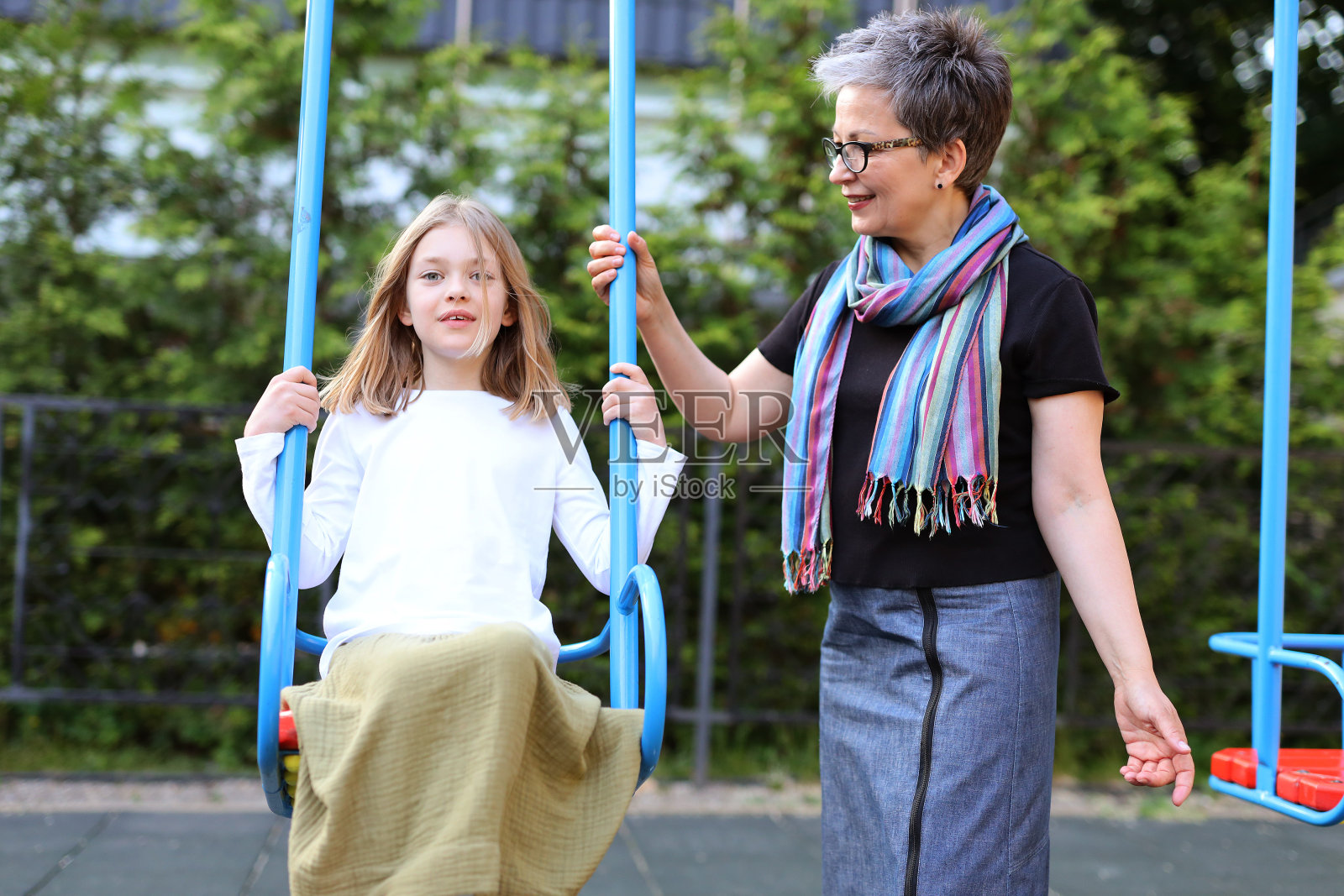 一个女孩和她的母亲或祖母在荡秋千。照片摄影图片