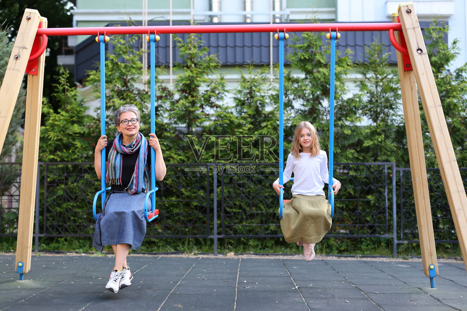 一个女孩和她的母亲或祖母在城市公园里荡秋千。照片摄影图片