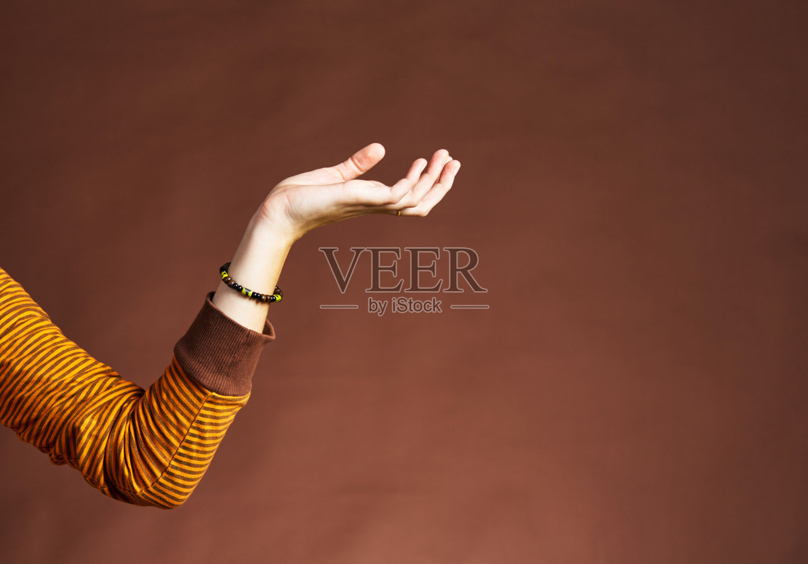 年轻女子将她的手伸到一个棕色的背景上,为你的物体或复制品留出空间照片摄影图片