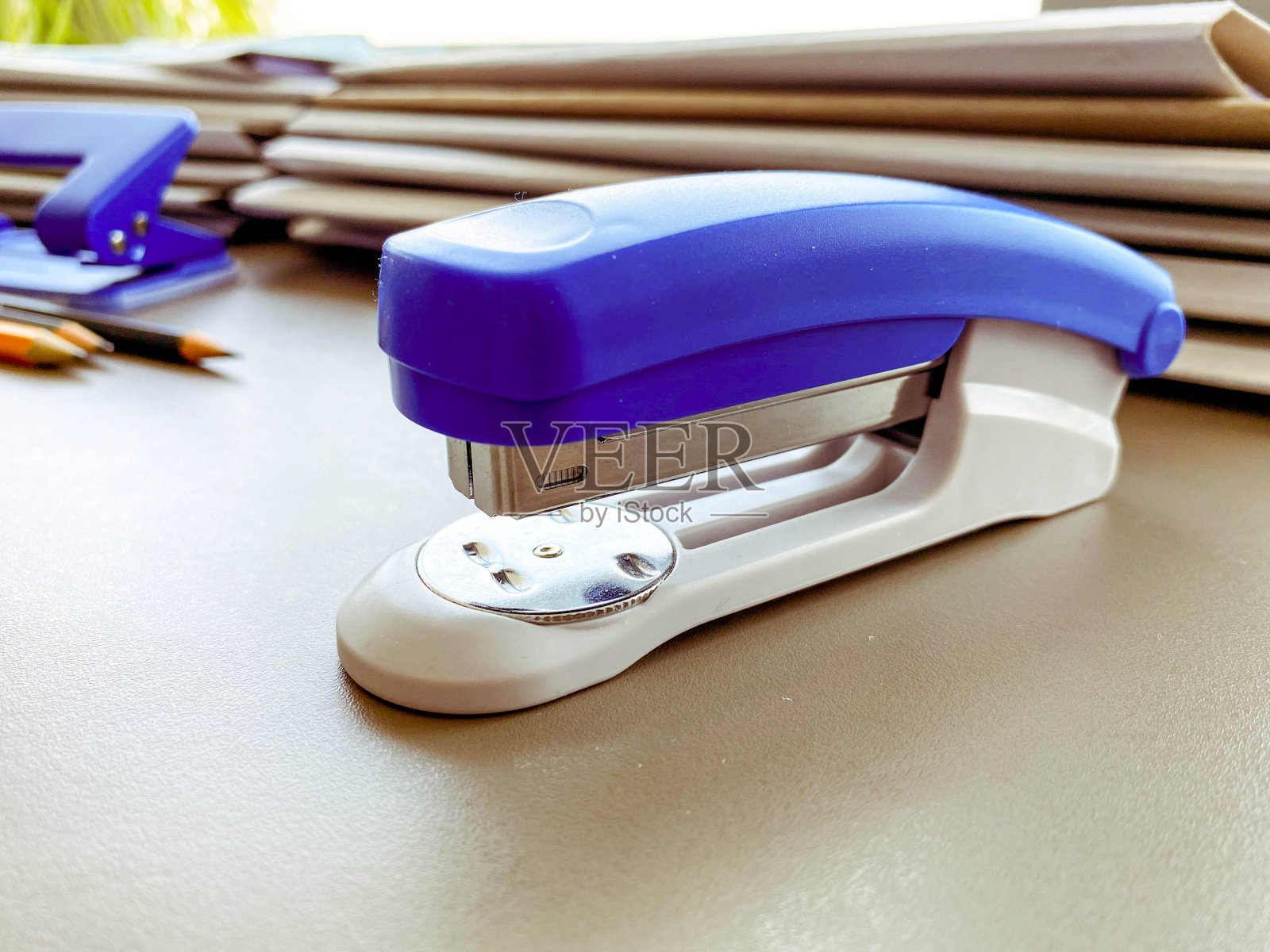 办公用品。蓝色订书机用于固定文件。文具在办公室的桌子上。订书机放在纸板文件夹旁边照片摄影图片