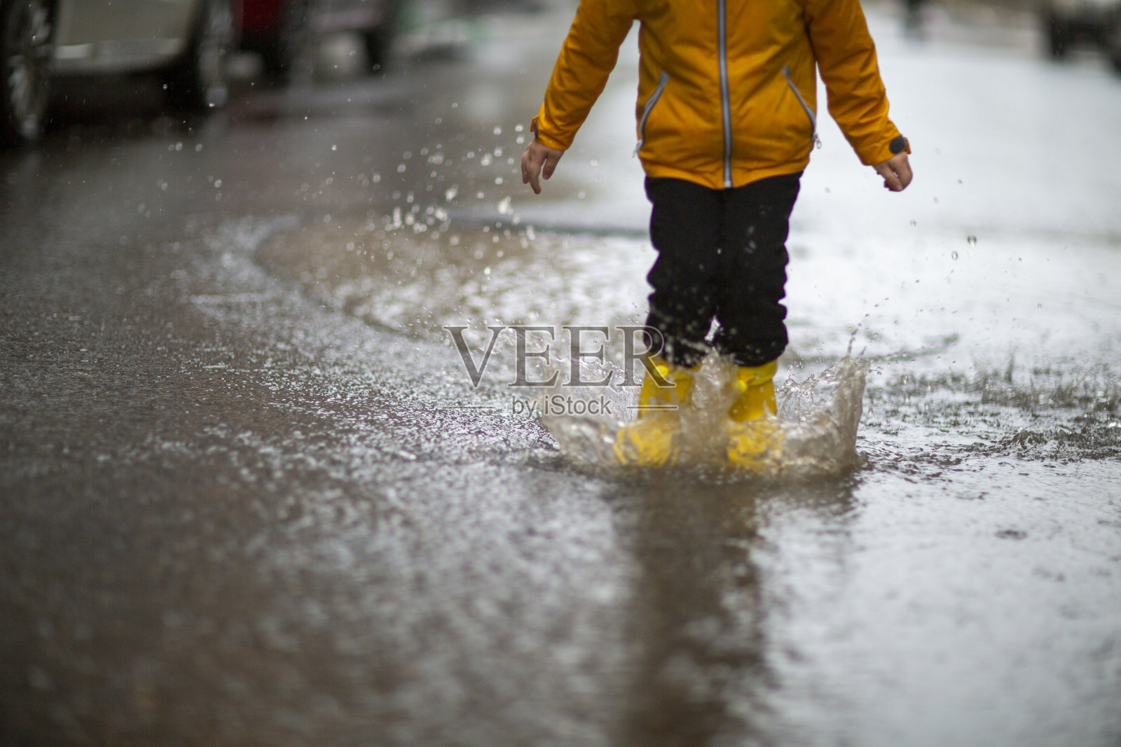 穿着黄色胶靴的孩子在水坑里跳跃的双腿照片摄影图片