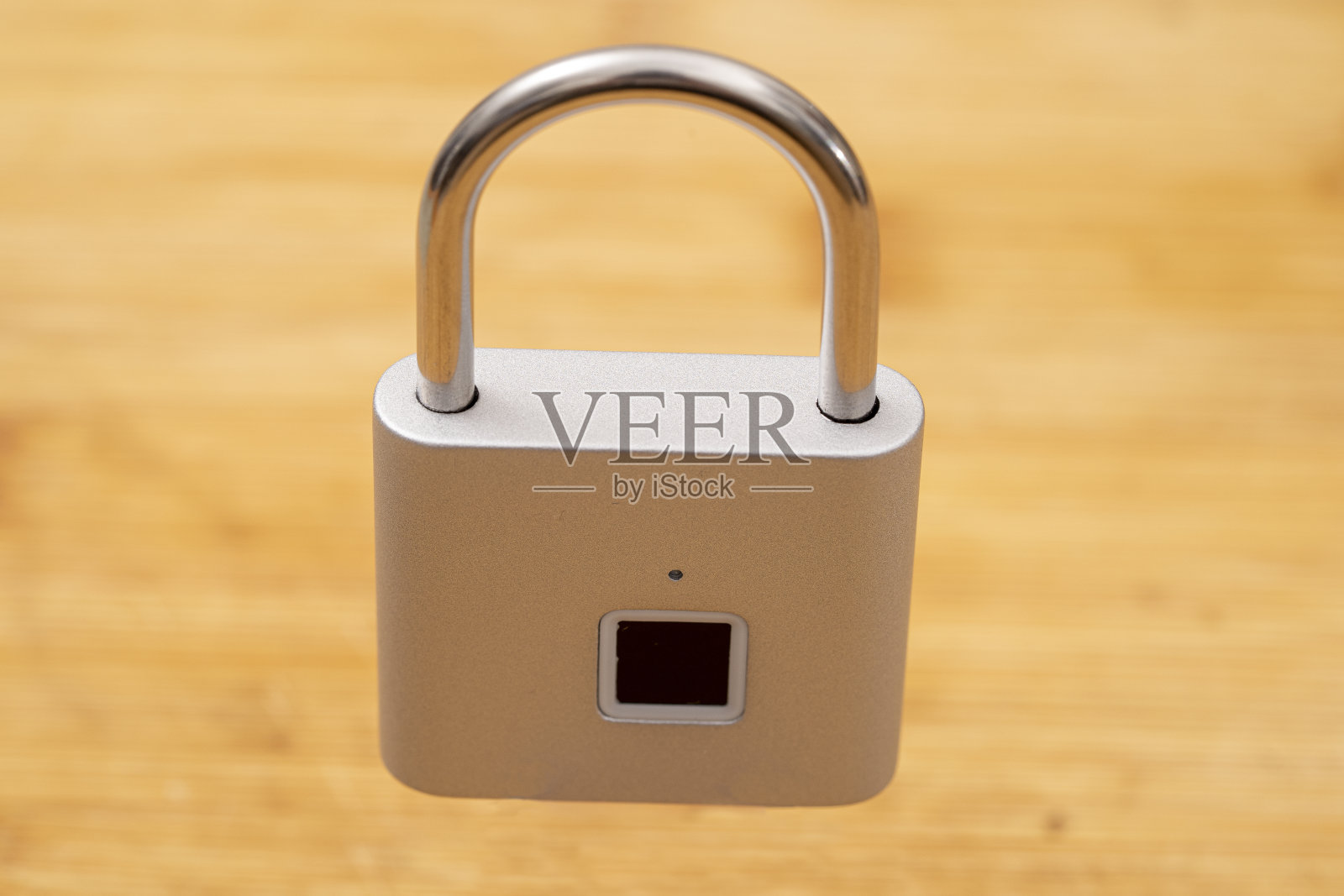 封闭式浅灰色挂锁,指纹开口。木色背景剪出。照片摄影图片