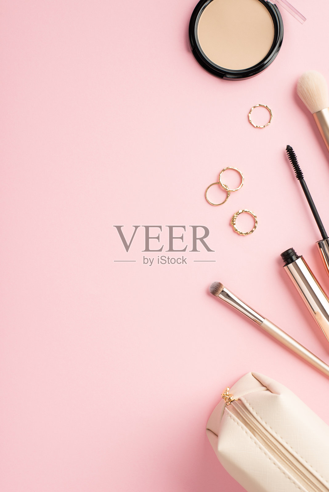 构成美的概念。俯视图垂直照片的金戒指紧凑的粉末化妆刷睫毛膏和化妆包在粉彩粉红色的背景与空白照片摄影图片