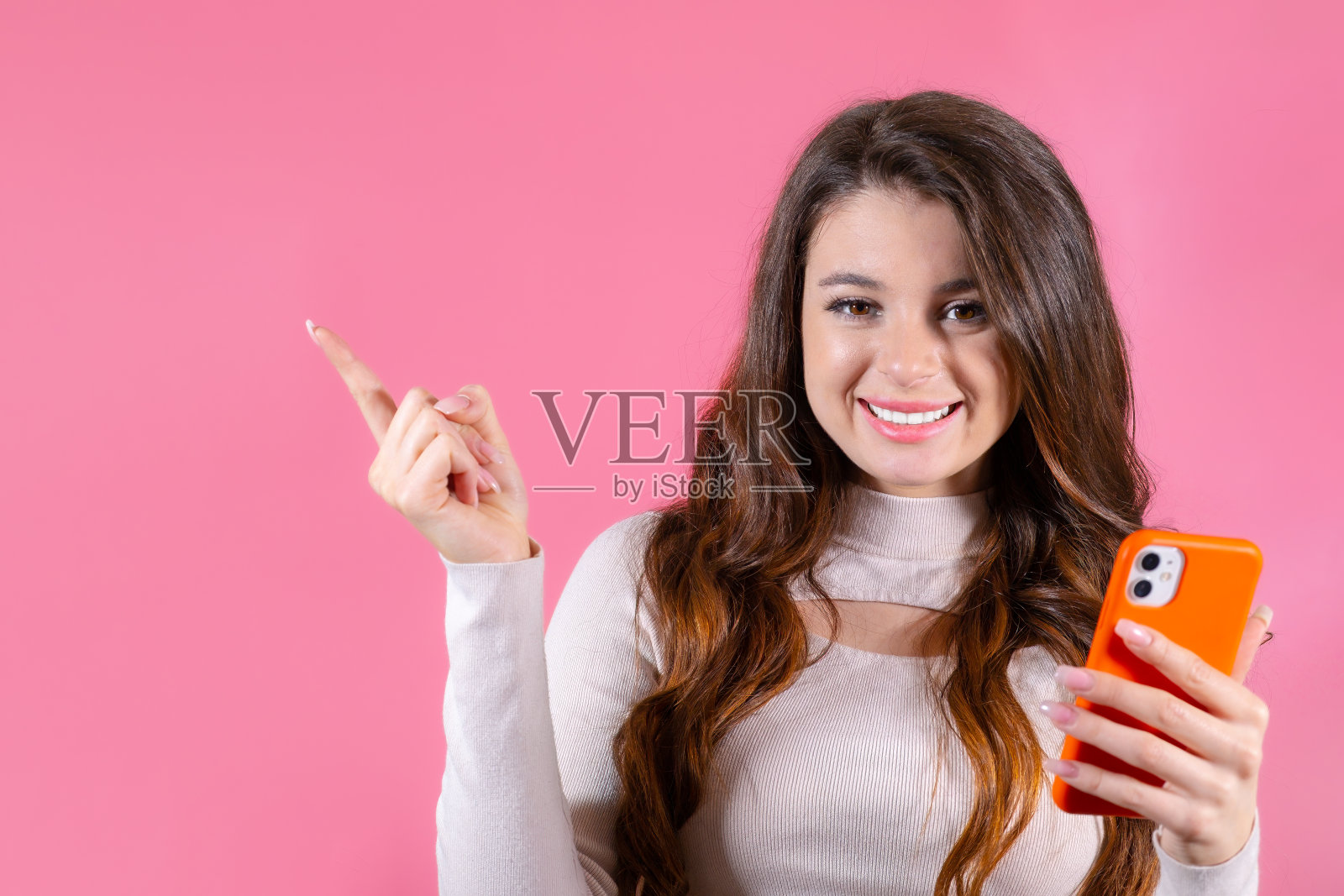 一个迷人的女人,带着灿烂的微笑,拿着一部手机,背景是醒目的粉红色照片摄影图片