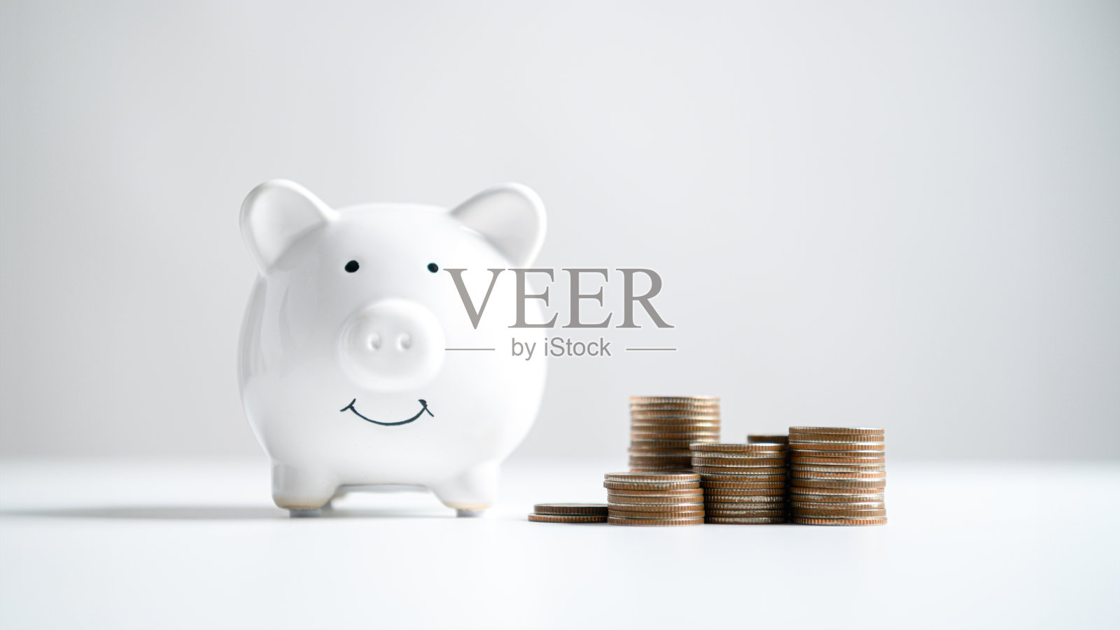 白色的小猪储蓄罐与堆叠的硬币背景。财务成功、金钱储蓄、计划货币和商业财富概念。照片摄影图片