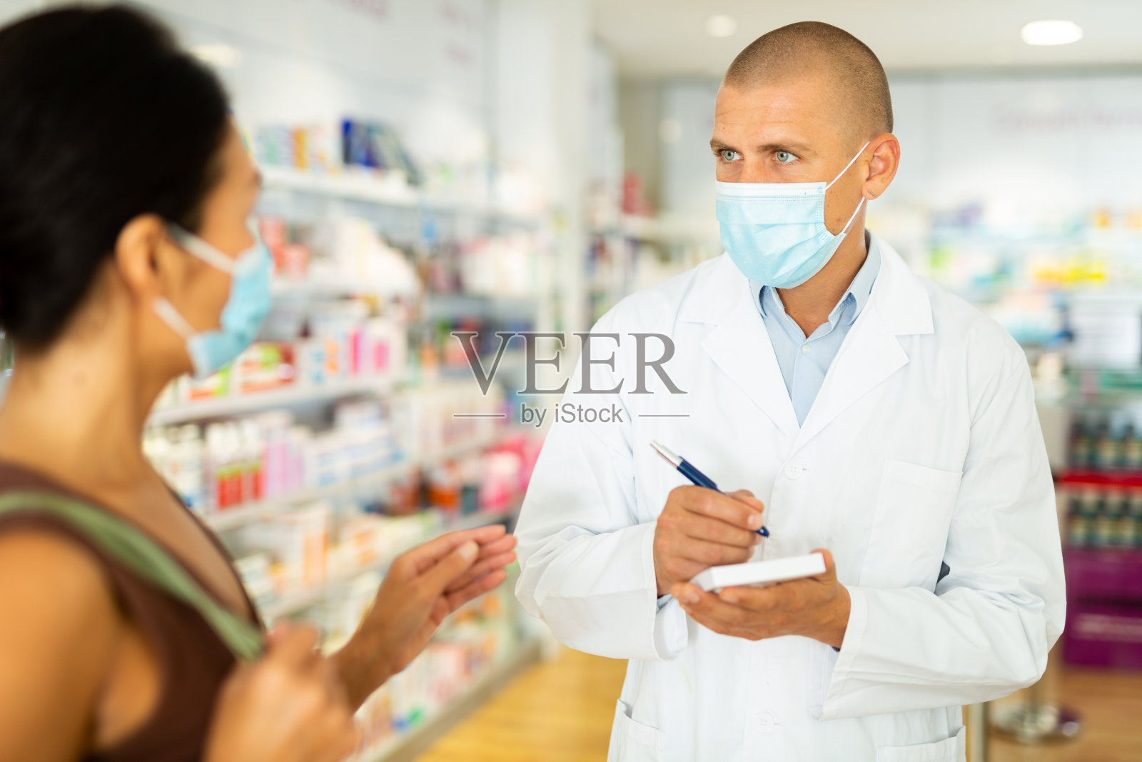 戴面具的药剂师正在和女人谈话,并在写处方照片摄影图片