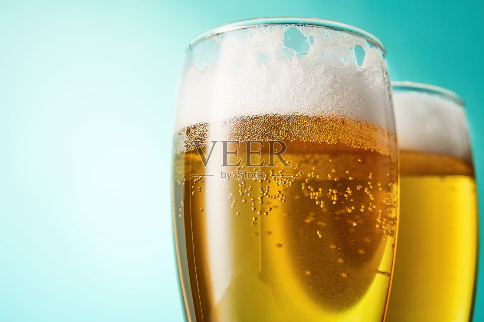 两杯淡蓝色背景的泡沫啤酒。照片摄影图片