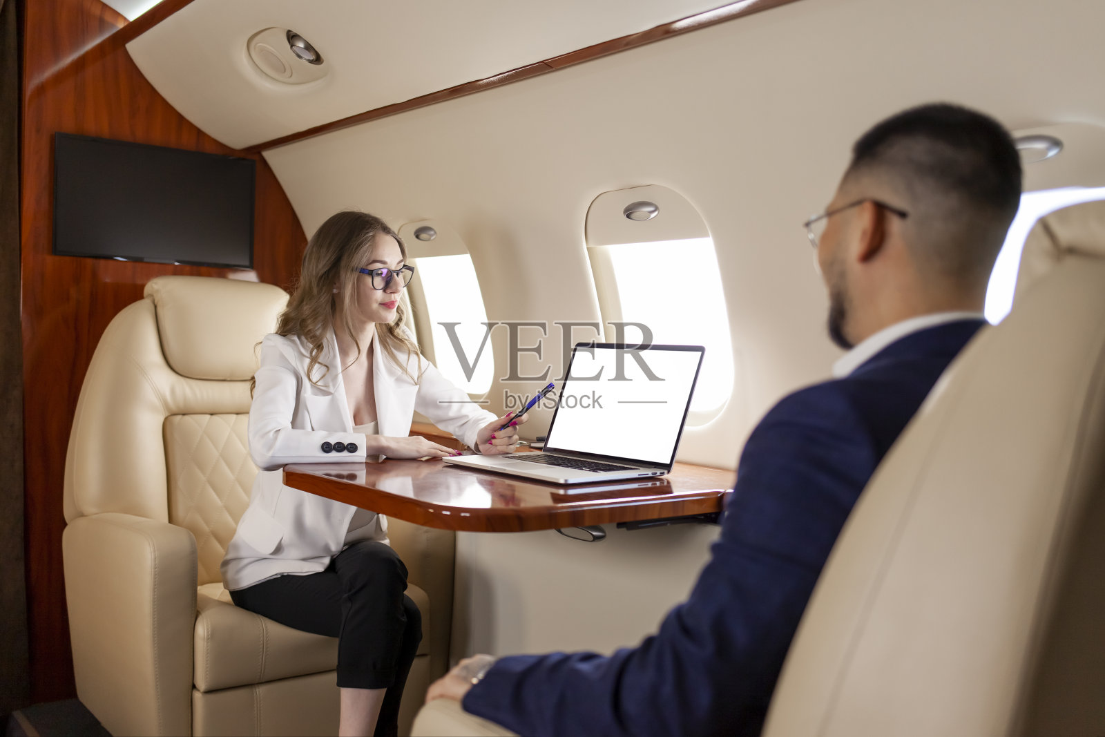 在飞机上开商务会议,西装革履的女商人指着空白的笔记本电脑屏幕与生意伙伴交谈照片摄影图片