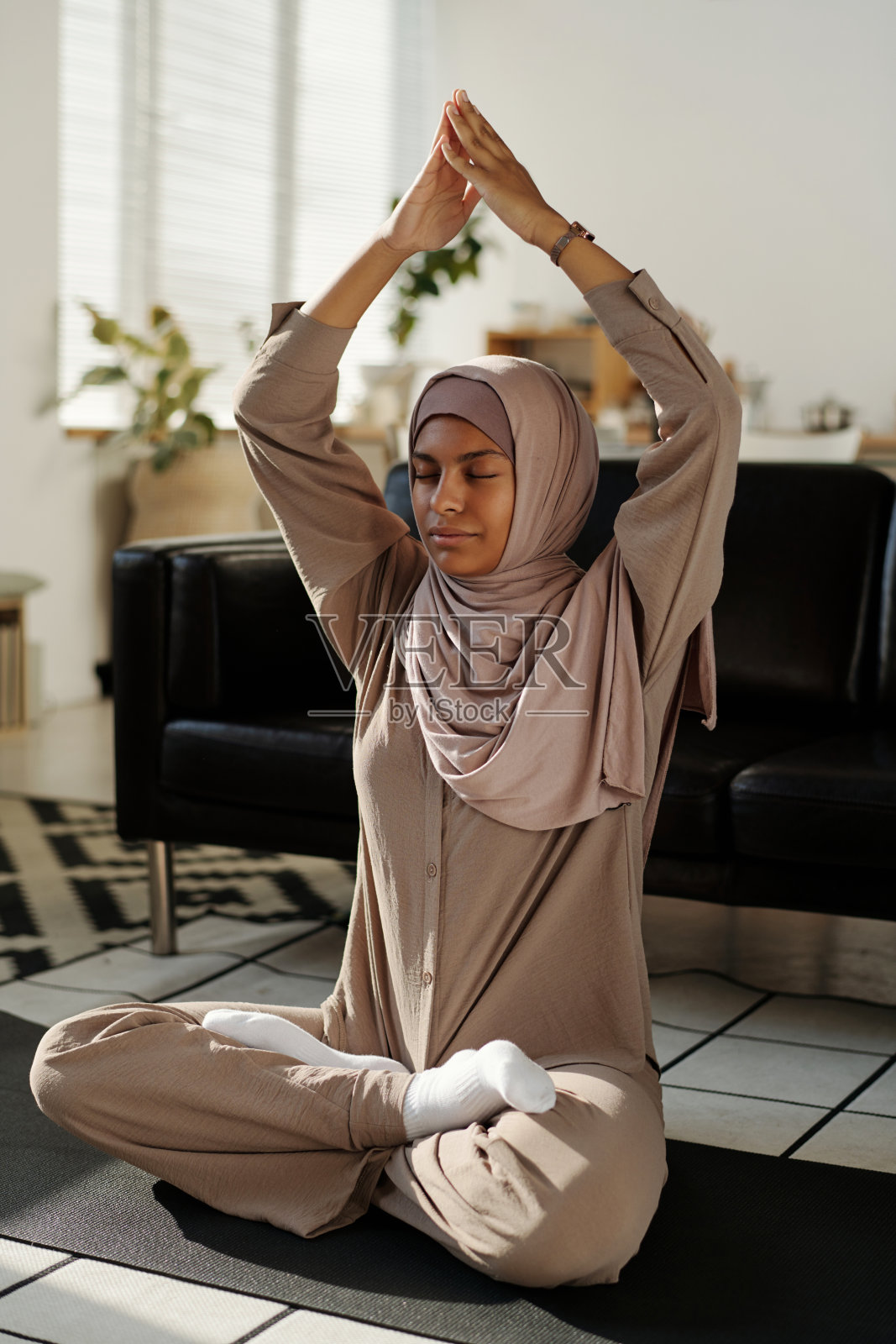 穆斯林妇女坐在莲花的姿势,她的双手放在一起在头上照片摄影图片