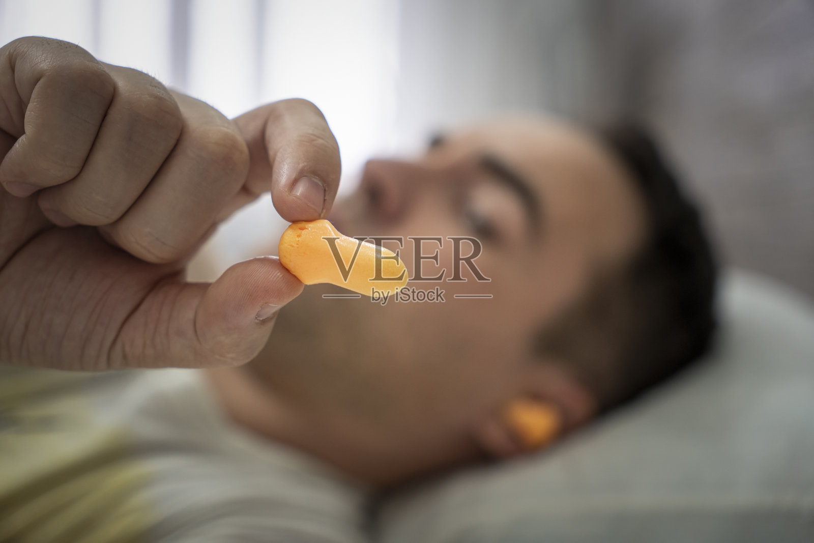 漂亮的年轻人熟睡着,耳朵里的橙色耳塞抵挡着街上的噪音,拯救着吵闹的邻居。当防止睡眠。睡觉时戴上耳朵,保持安静。照片摄影图片