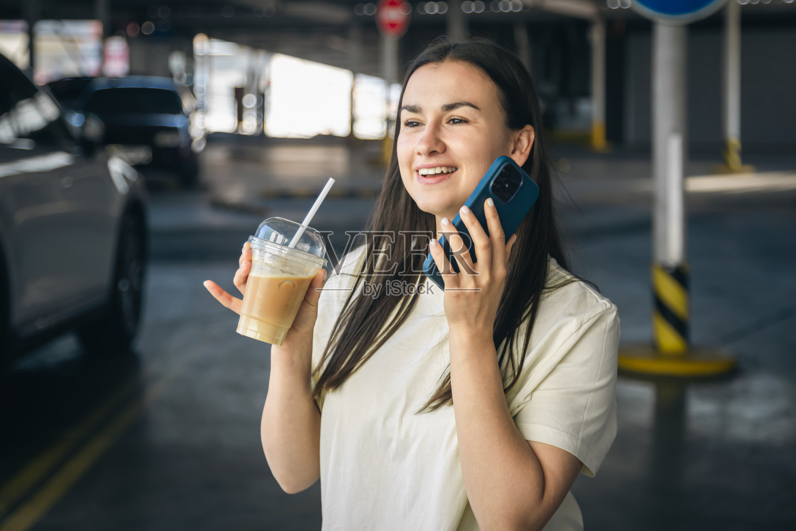 一个喝着咖啡的年轻女人在停车场打电话。照片摄影图片