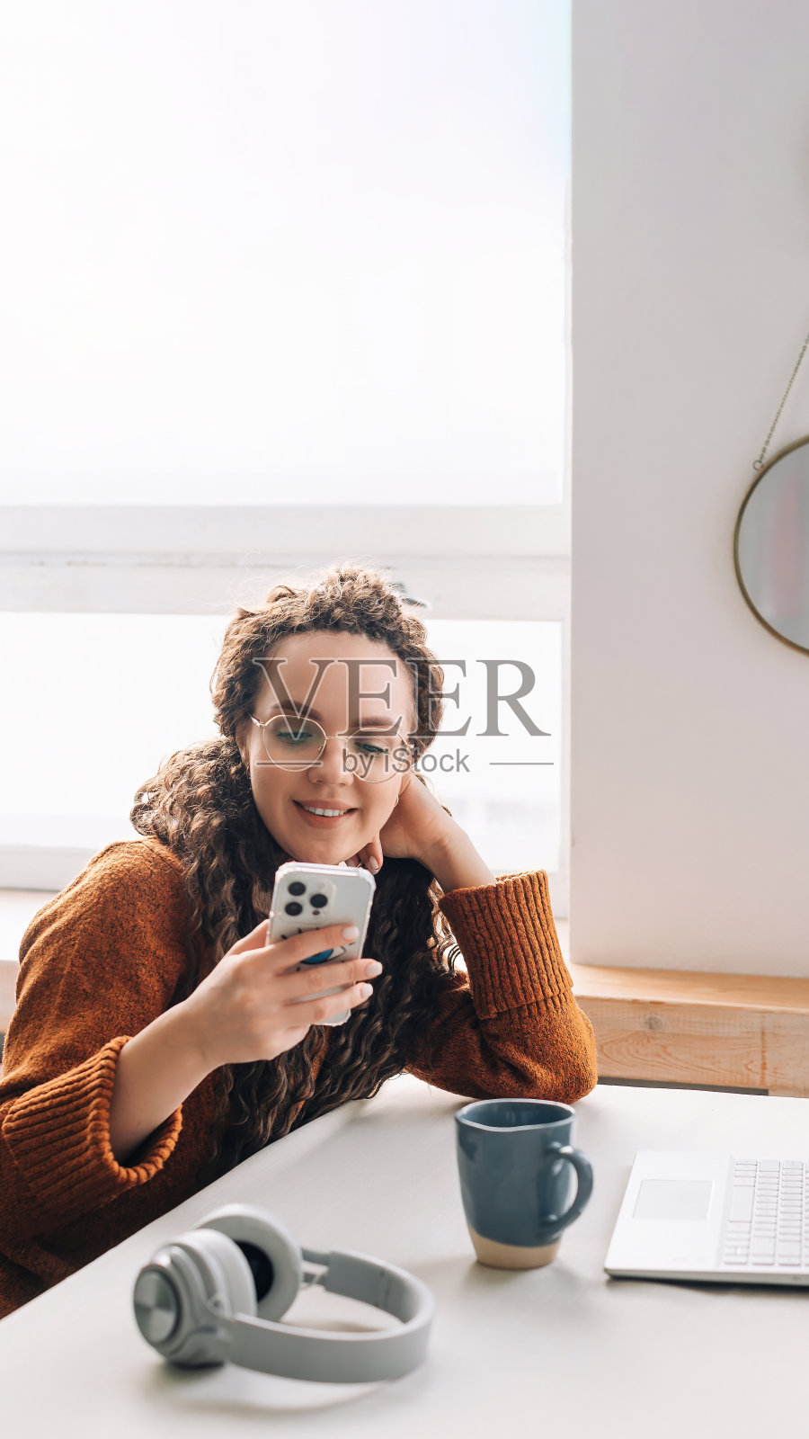 微笑的年轻女子在家里远程工作时发短信,办公技术和现代生活方式的概念。快乐的年轻女性使用智能手机在家庭办公室远程工作和学习照片摄影图片