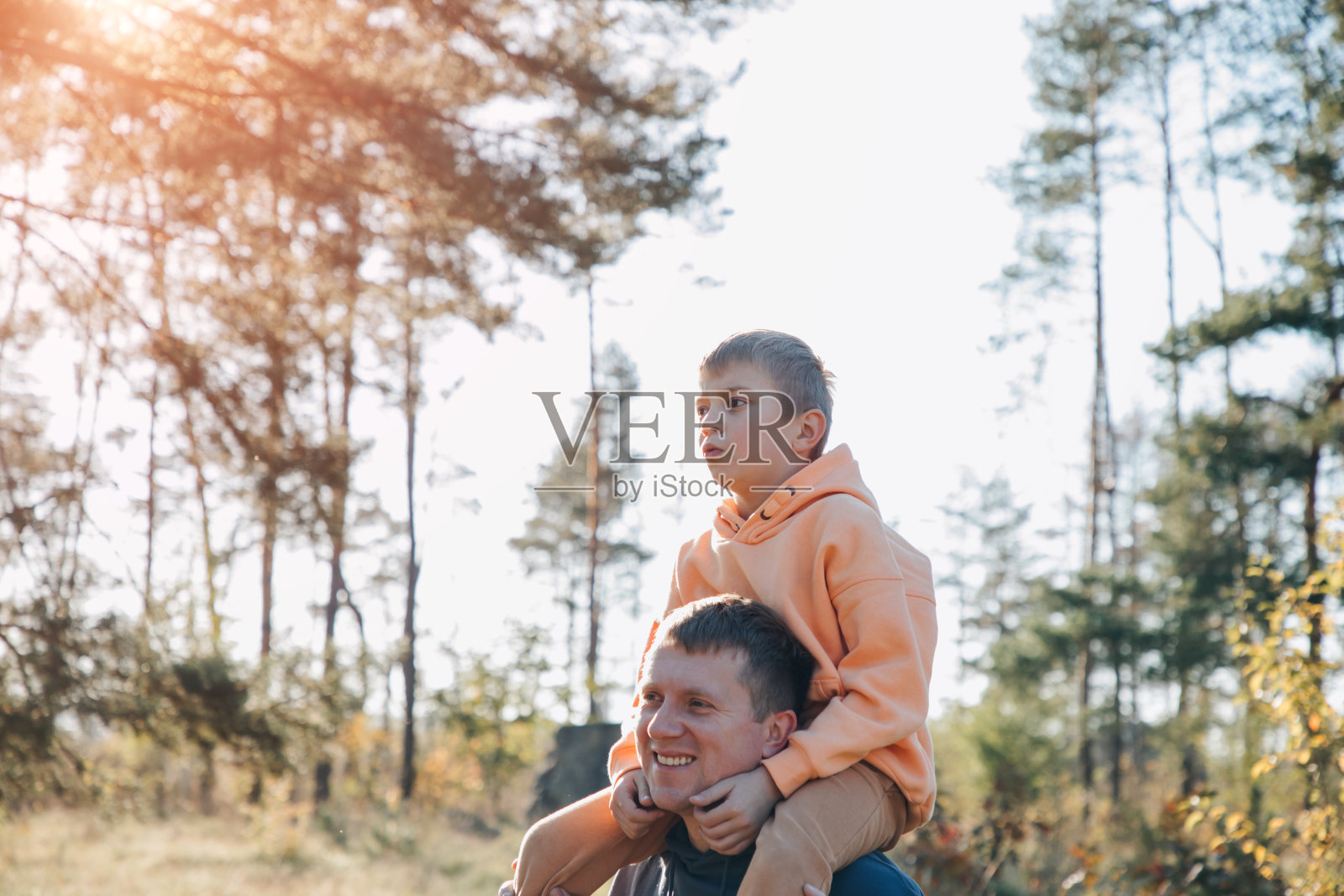 爸爸和儿子在阳光明媚的森林里散步。家庭休闲。父亲把儿子扛在肩上照片摄影图片