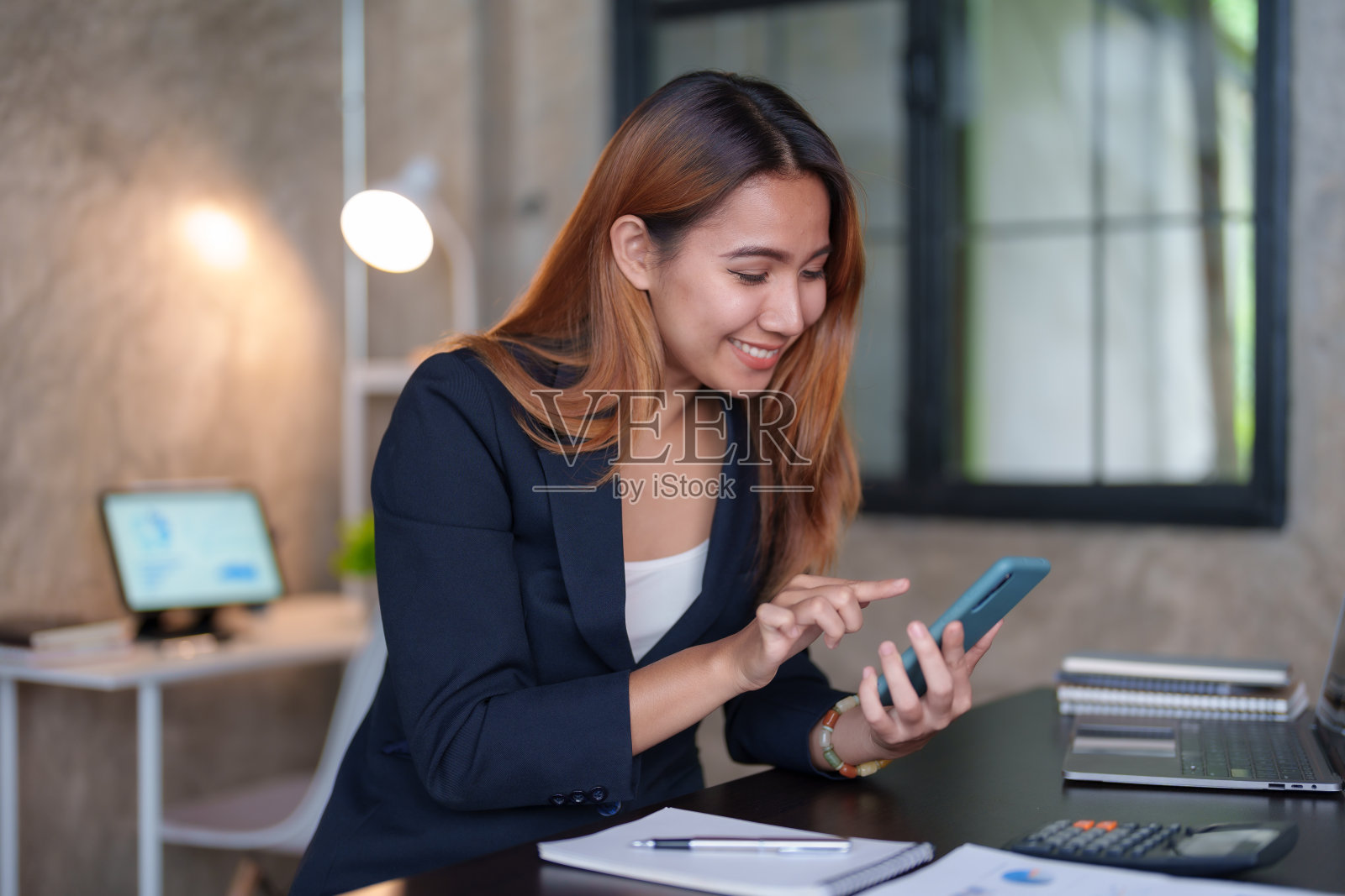 美丽的亚洲女商人在办公室用智能手机联系客户,回复聊天,在社交媒体应用程序上交易,脸上带着微笑。照片摄影图片