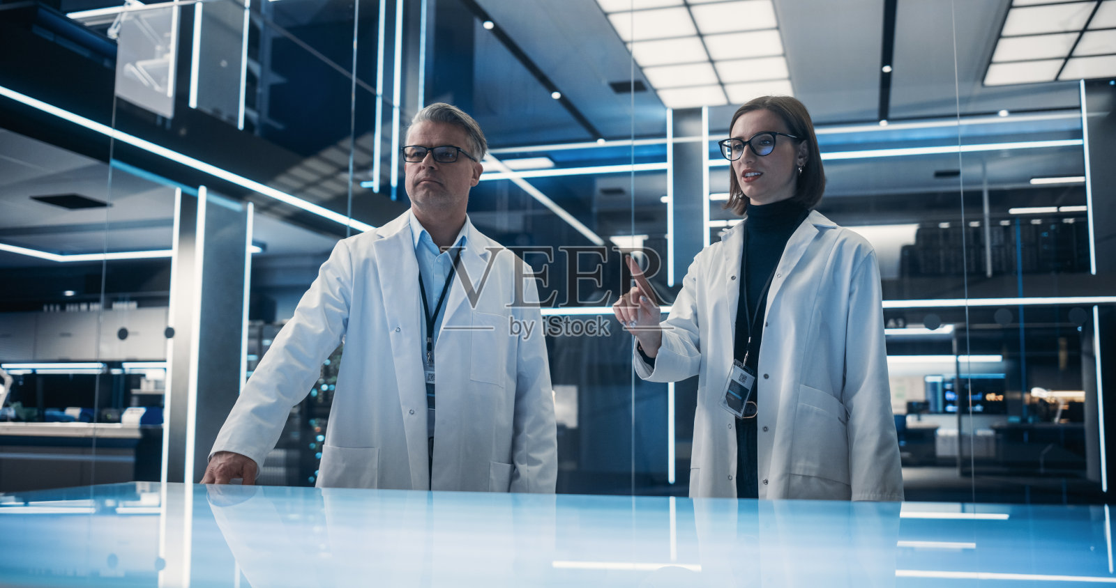 站在高科技实验室桌子旁边的白人男女科学家。专业的工业工程师在桌子上打手势。增强现实编辑的模型模板。照片摄影图片