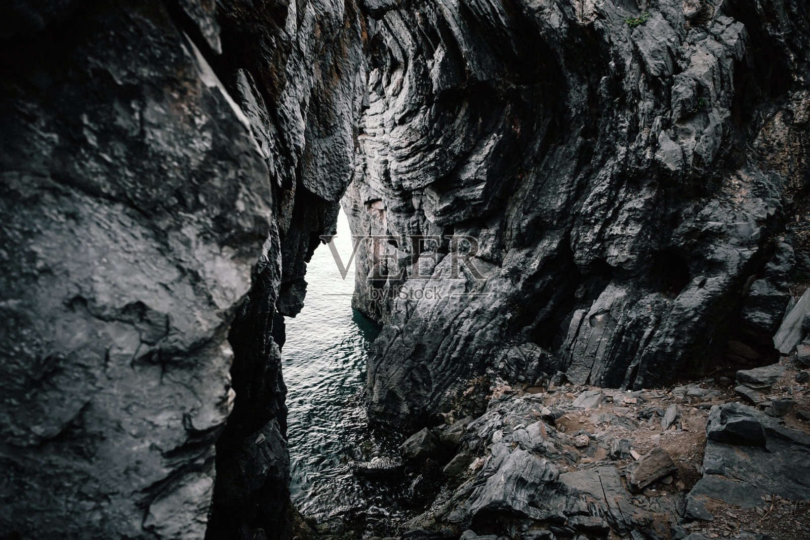 海岸上拍摄的锈迹斑斑的风化织物的大框架 岩石峭壁和一小块海面照片摄影图片