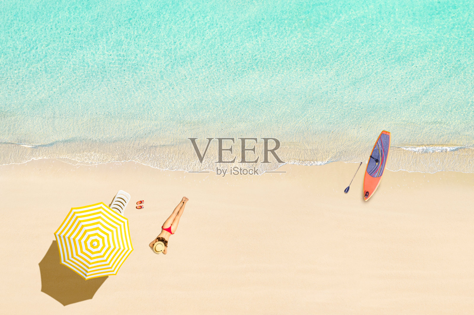 在热带塞舌尔的沙滩上,穿着比基尼的女人躺在伞下晒太阳,用SUP板冲浪。航拍、无人机视图照片摄影图片