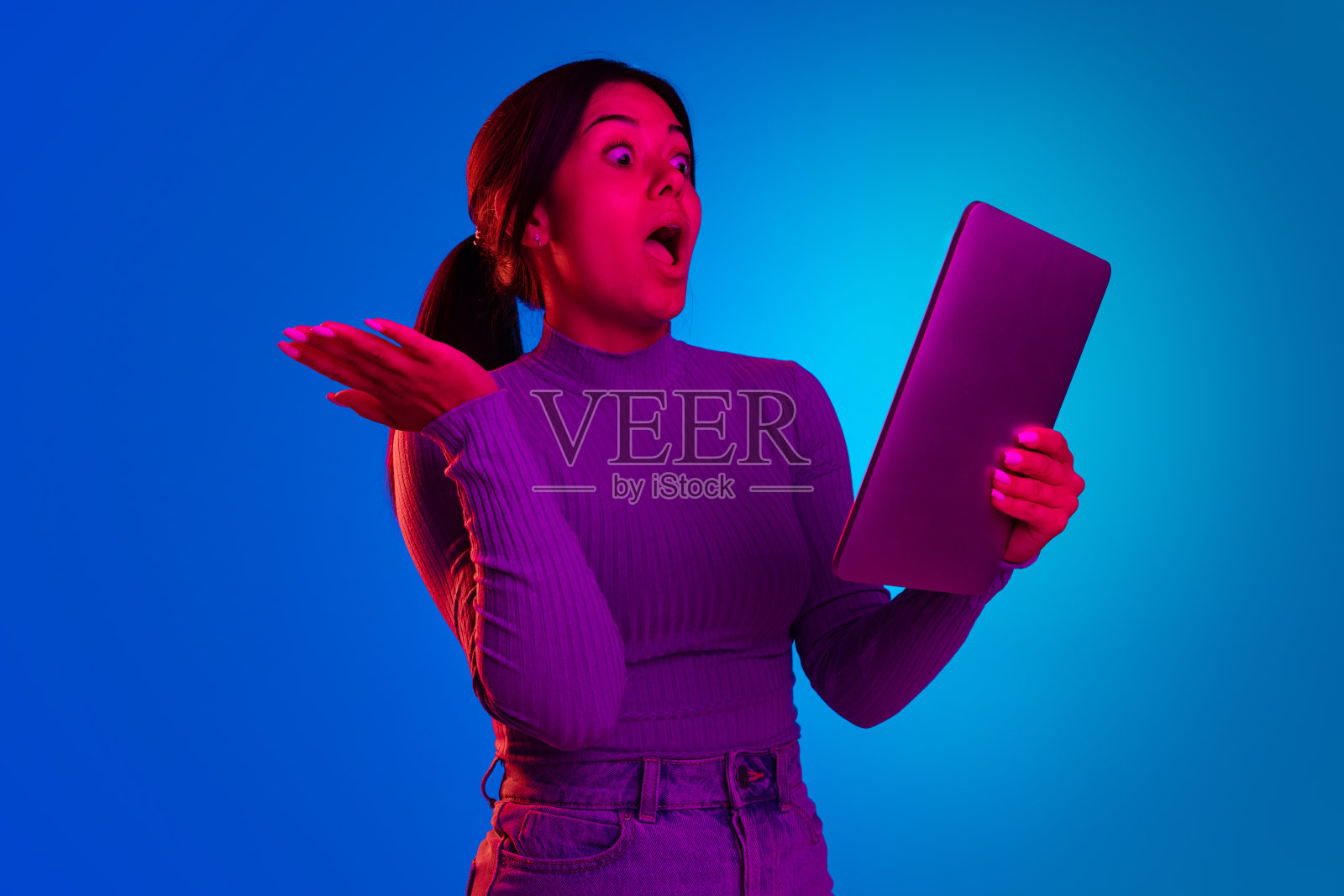 年轻的情感女孩的肖像有在线视频电话的平板电脑孤立在蓝色背景下的霓虹灯照片摄影图片