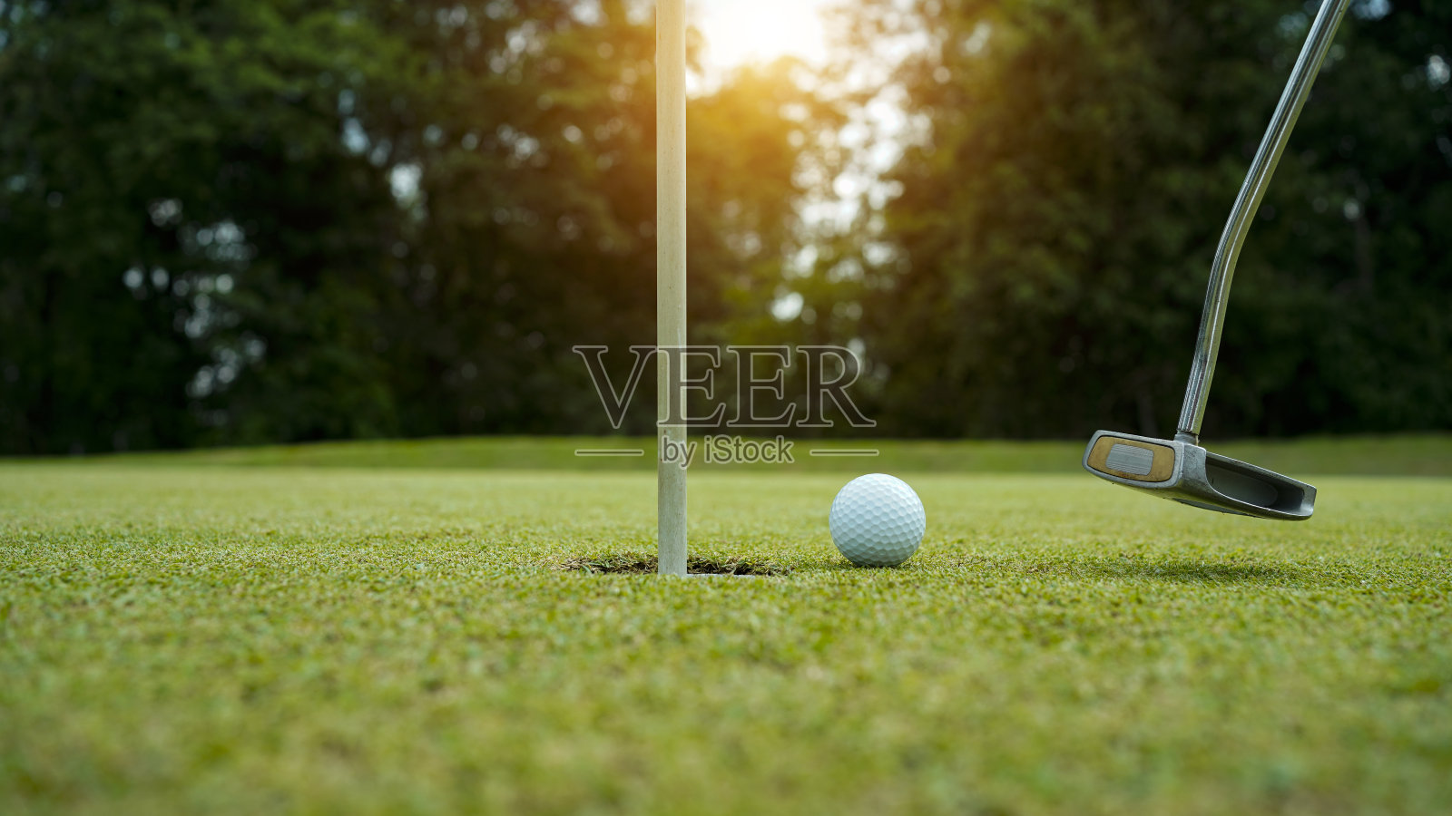 高尔夫球将在日落时分由高尔夫球手在绿草高尔夫球场打洞。照片摄影图片