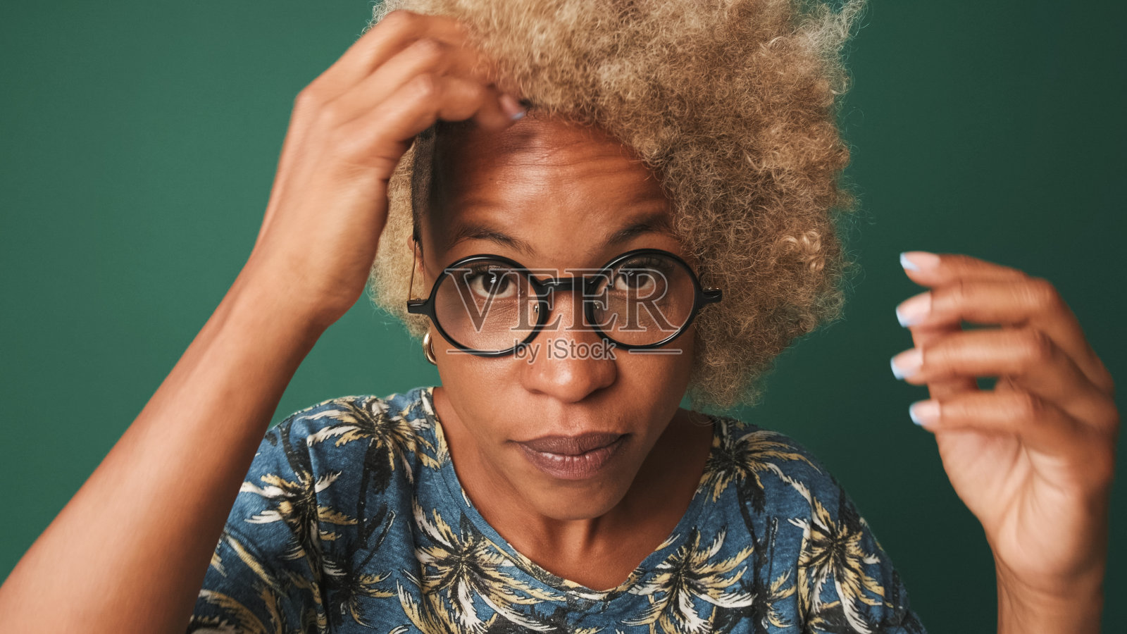 一个戴着眼镜,穿着蓝色t恤的女孩的特写,看着镜头,像在镜子里一样,拉直她的头发,孤立的绿蓝色背景照片摄影图片