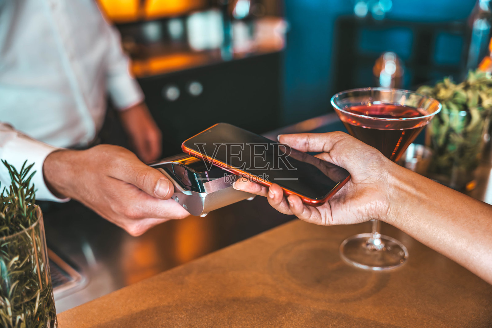 一位女士在餐厅用近距离通信技术用智能手机付账——满意的顾客用非接触式技术用智能手机付账——酒吧大厅用手机支付的特写镜头照片摄影图片
