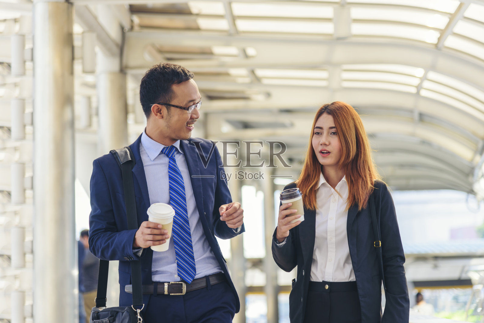在现代城市办公室外小镇喝咖啡的男女商人。手拿外卖咖啡杯,愉快地交谈。穿着正装、拿着咖啡杯的商务伙伴照片摄影图片