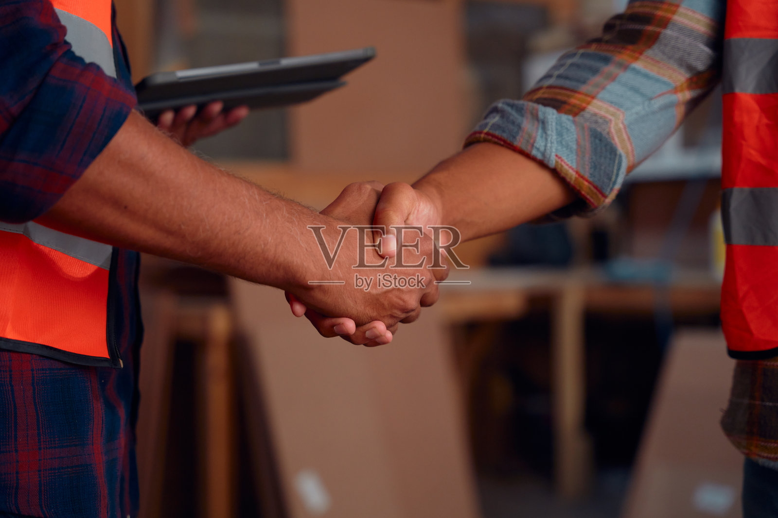 木工工厂里,同事们穿着反光服握手的特写照片摄影图片