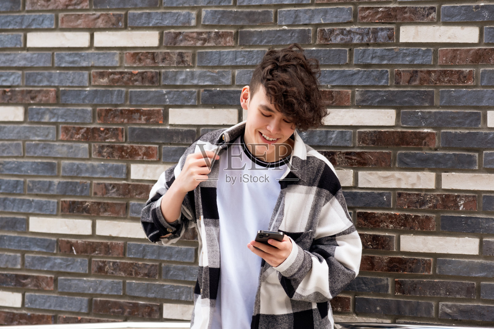 一个年轻人靠着砖墙读着有趣的电话留言照片摄影图片