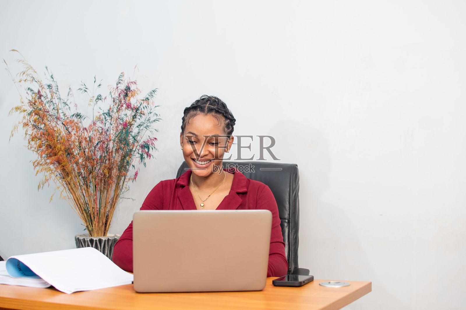 一个快乐的非洲女人坐在桌子前用笔记本电脑工作。照片摄影图片