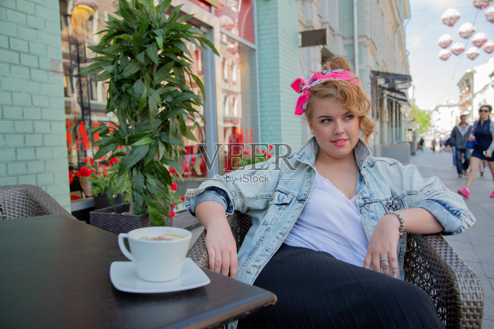 这个女孩正坐在街边咖啡馆的桌旁。春天,美丽的大码模特在街上的咖啡馆里喝咖啡。照片摄影图片