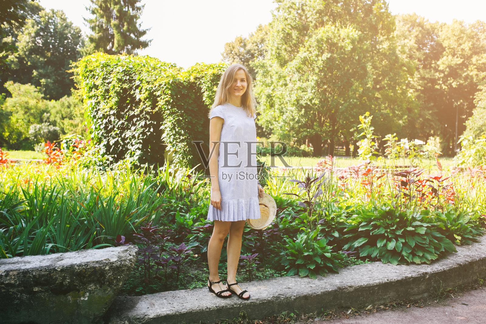 漂亮的女孩穿着时髦的裙子,戴着时髦的帽子,在公园里散步。夏天快乐地在户外拍照。照片摄影图片