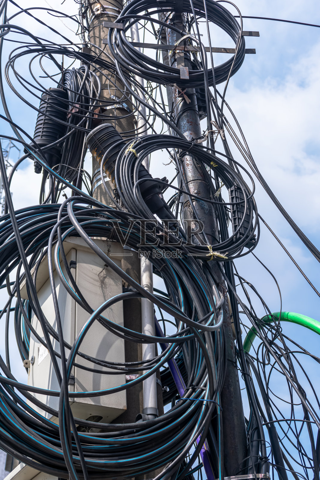 在清澈明亮的蓝天下,杂乱的电缆在电线杆上滚动照片摄影图片