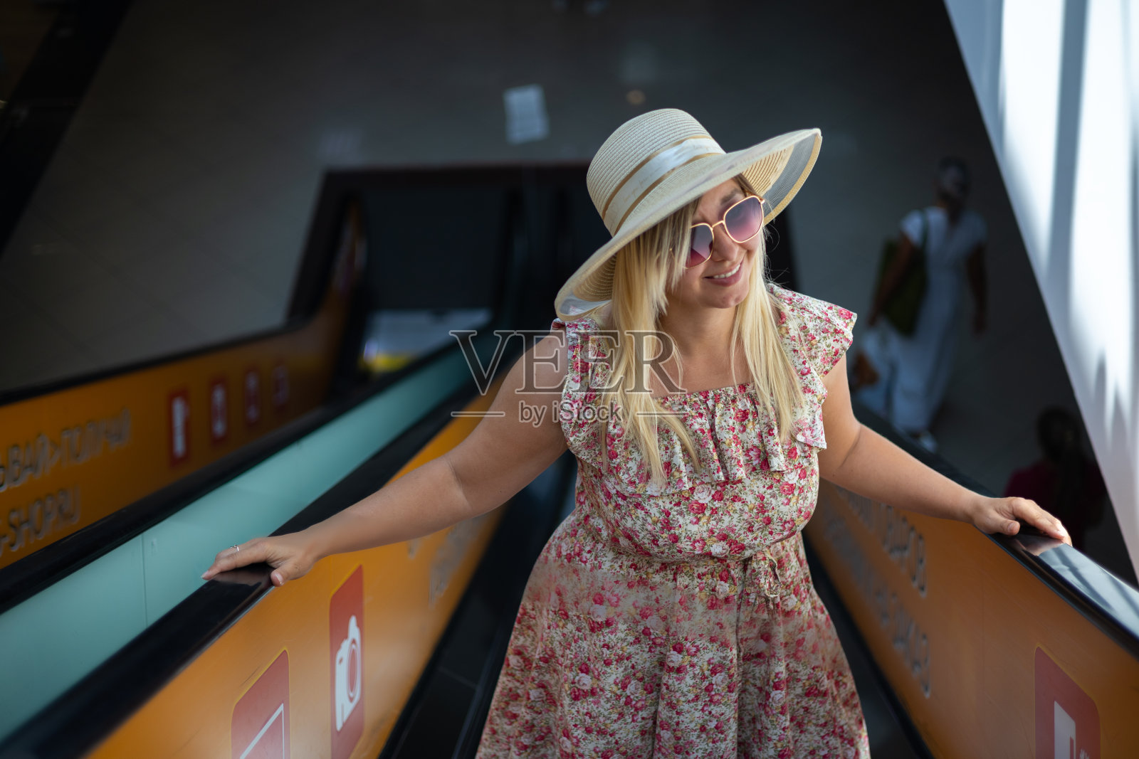 在一个炎热的夏日,一位美丽的女人正在享受购物中心之旅。一名妇女爬上购物中心的自动扶梯楼梯,目光转向别处。概念夏季肖像在商场。照片摄影图片