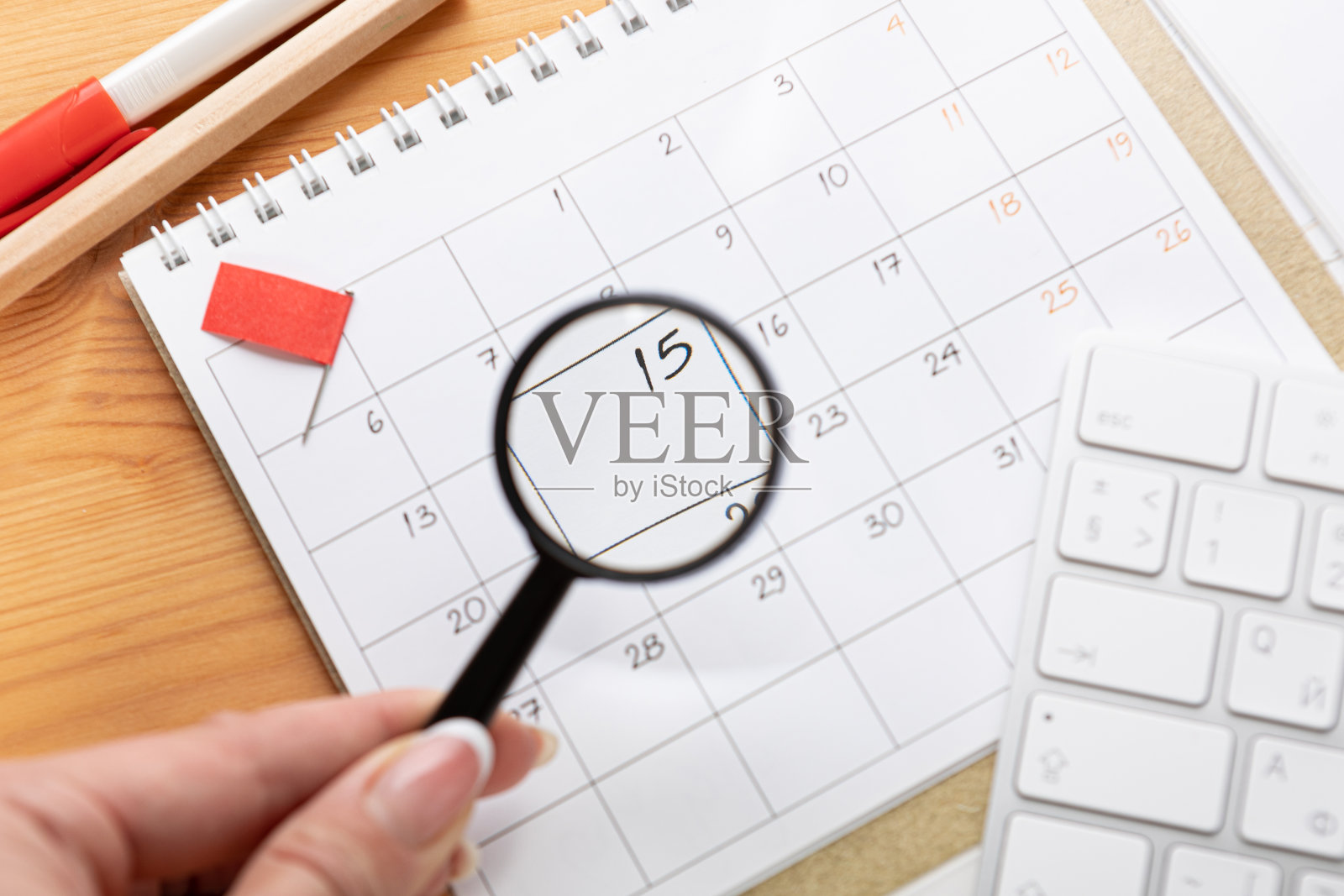 一只拿着放大镜的手在网上检查日历和工作提醒。滑翔机桌面上有鼠标和笔,键盘。把假期旅行或计划记在办公桌上的日记本上。2023日历提醒概念。照片摄影图片